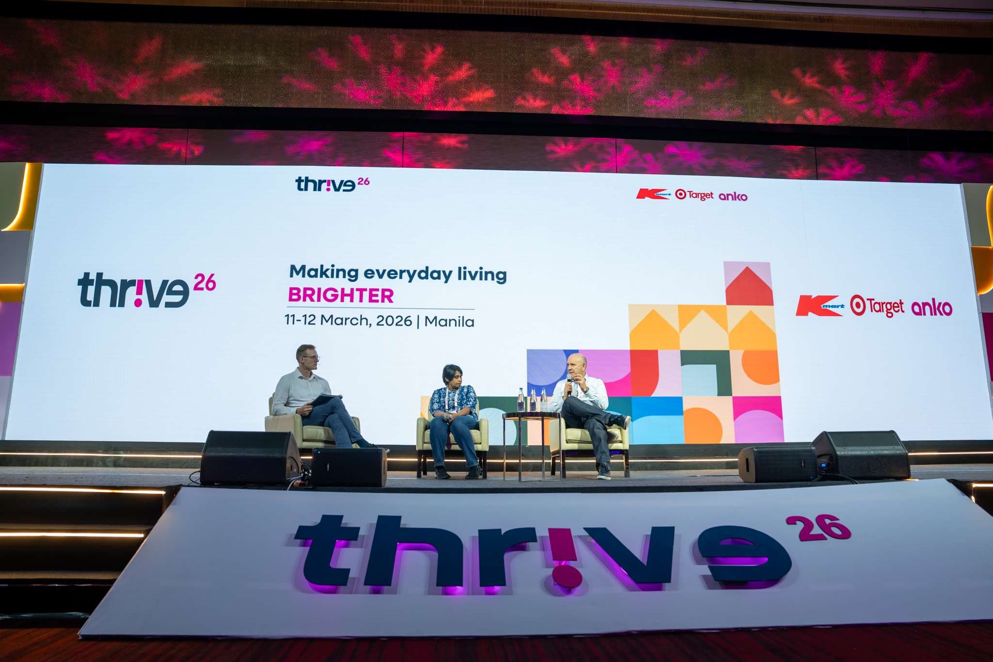 Three panellists in conversation on the Thrive main stage at Grand Hyatt Manila, the full 'Making everyday living BRIGHTER' branding and the Kmart, Target and anko logos on screen behind them, the thrive26 stage signage in the foreground