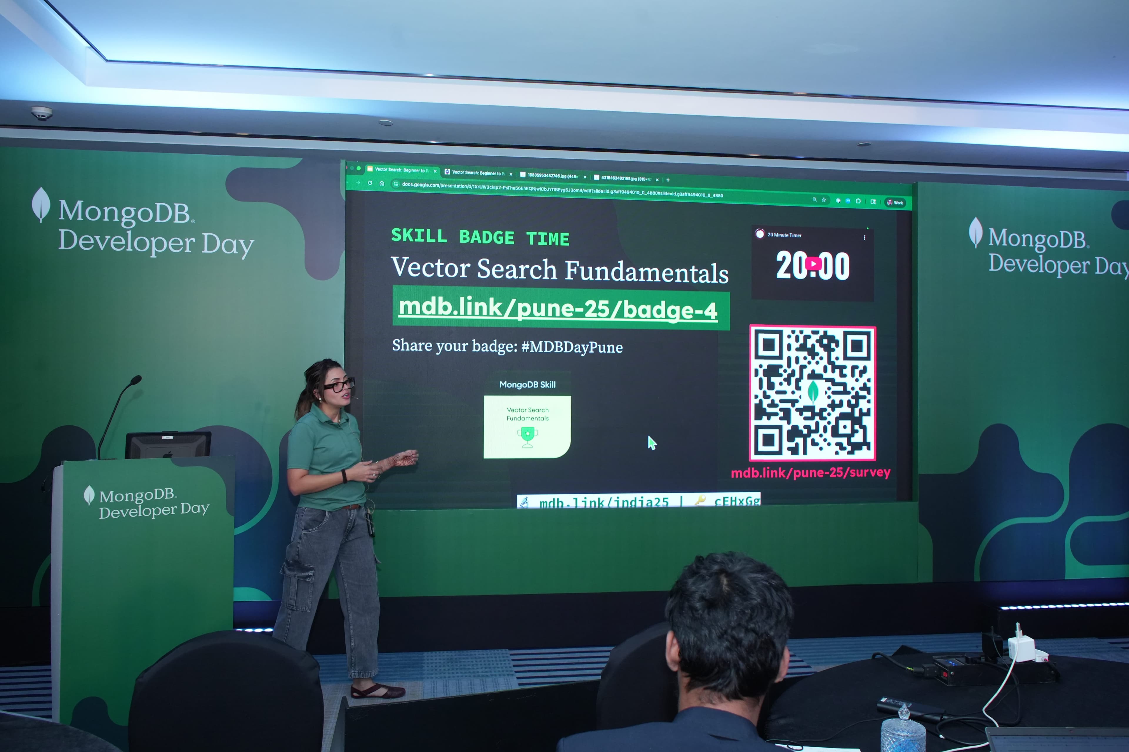 A MongoDB Developer Day presenter walks through a 'Skill Badge Time: Vector Search Fundamentals' exercise, a twenty-minute countdown timer and a QR code to claim the badge on the screen behind her